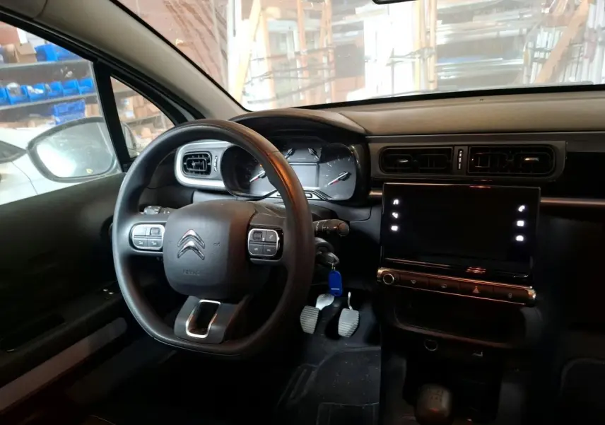 Intérieur avant de la Citroën C3 blanc banquise, volant multifonction, tableau de bord avec écran tactile et pédales visibles.