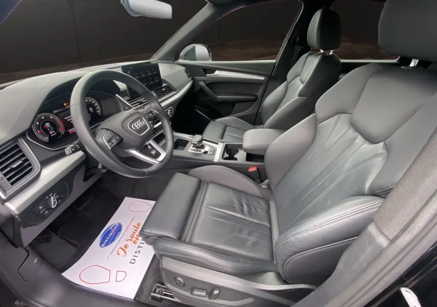 Vue intérieure côté conducteur de l'Audi Q5 Business Edition S-Line 2022 avec sièges sport cuir noir et tableau de bord digital.