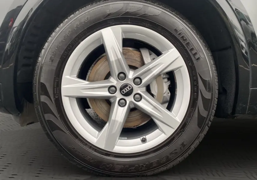 Gros plan sur la roue avant droite noire d’un Audi Q5 2022 avec jante alliage argentée à cinq branches.