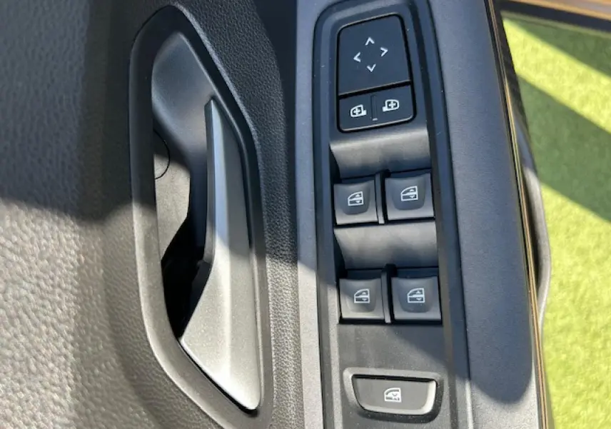 Gros plan sur la commande des lève-vitres et rétroviseurs côté conducteur de la Dacia Sandero beige Safari.