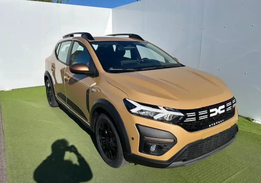 Vue 3/4 avant droite d'une Dacia Sandero III Stepway beige Safari avec calandre noire et jantes noires.