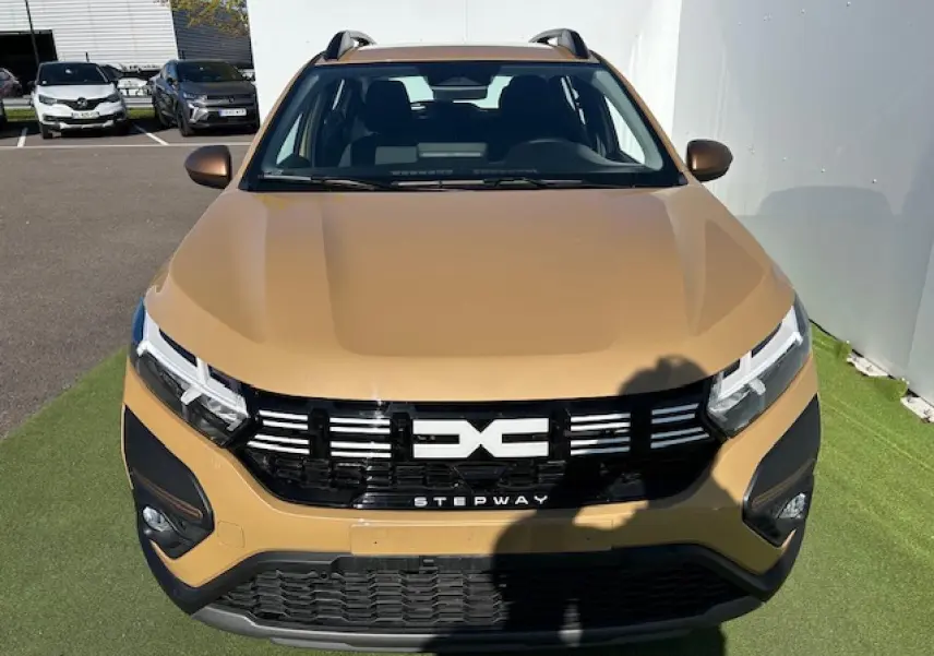 Vue avant d'une Dacia Sandero III Stepway beige Safari avec calandre noire et logo central blanc Stepway.