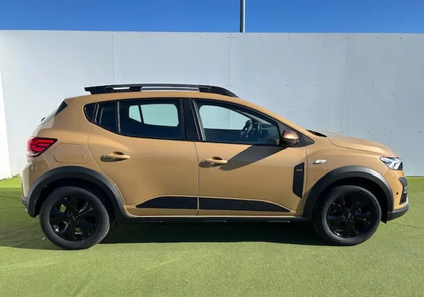 Profil droit d'une Dacia Sandero Stepway beige Safari avec jantes noires et barres de toit noires brillantes.