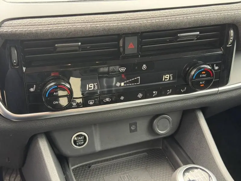 Détail du tableau de bord noir du Nissan Qashqai blanc nacré 2025, avec commandes climatisation digitale et bouton start/stop visible.