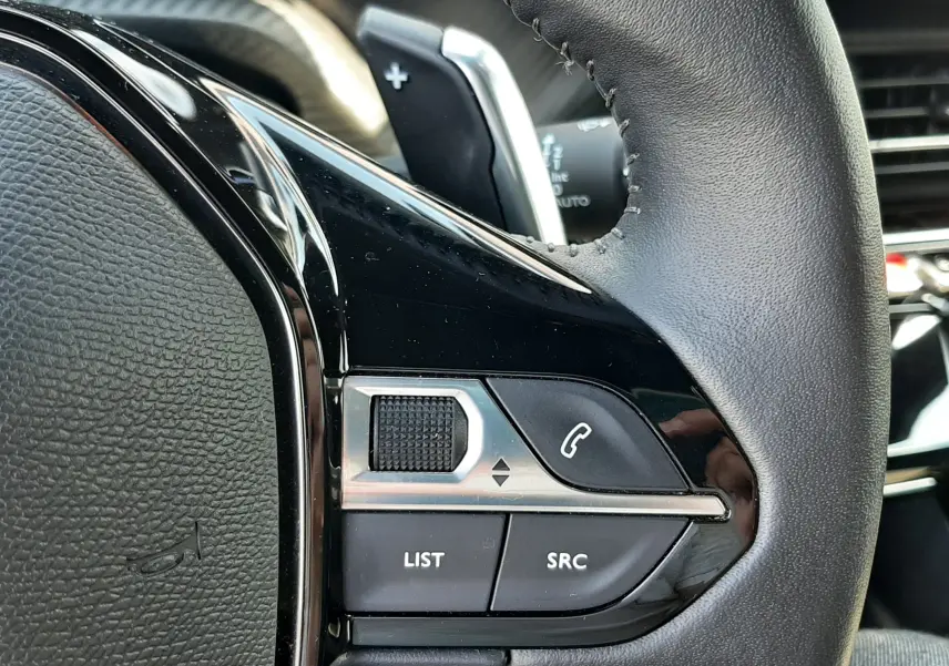 Gros plan sur les commandes gauche du volant cuir noir du Peugeot 2008 gris platinium, avec boutons multifonctions et palettes.