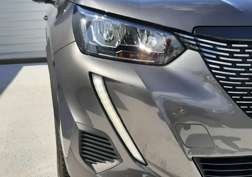Gros plan sur l'avant gauche du Peugeot 2008 gris platinium, mettant en valeur son phare LED et la calandre distinctive.