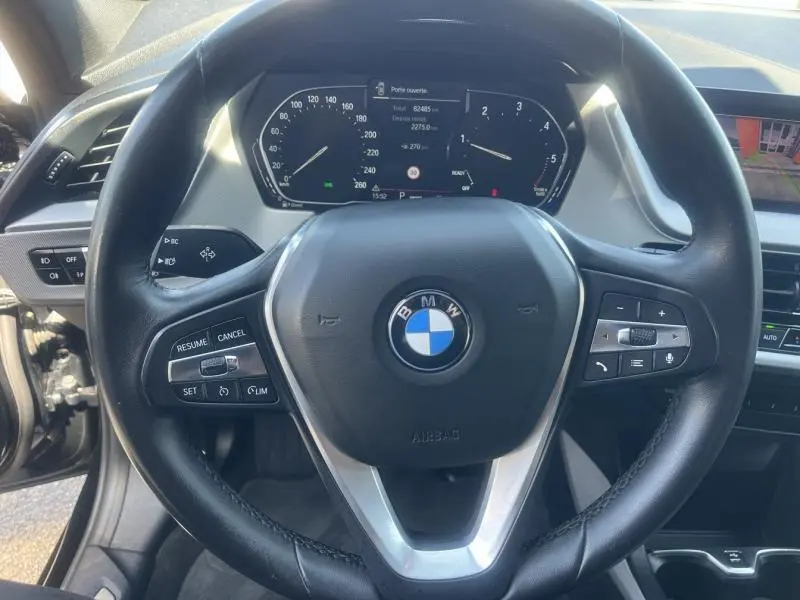 Vue rapprochée du volant cuir multifonction BMW Série 1 116dA 2020 avec tableau de bord numérique allumé.