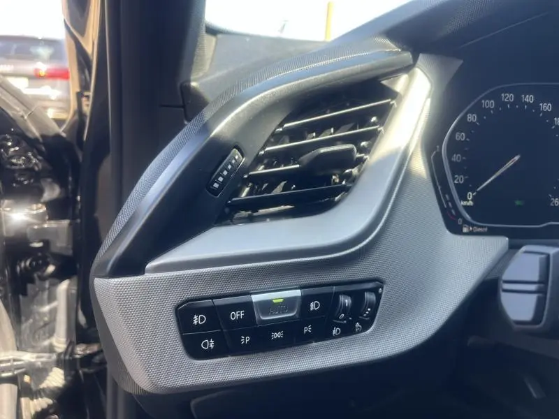 Détail du tableau de bord côté gauche d'une BMW Série 1 noire 2020, avec commandes d'éclairage et ventilation.