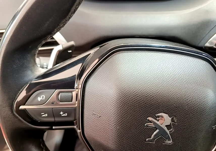 Gros plan sur le volant cuir noir du Peugeot 3008 2022 avec commandes multifonctions et logo lion central.