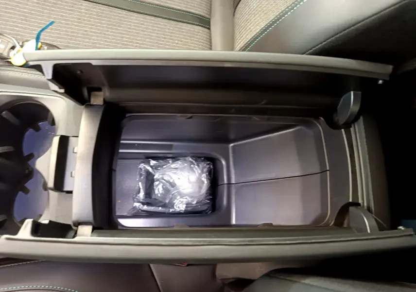 Vue plongeante sur la console centrale ouverte du Peugeot 3008 noir, montrant un rangement intérieur avec un objet emballé.