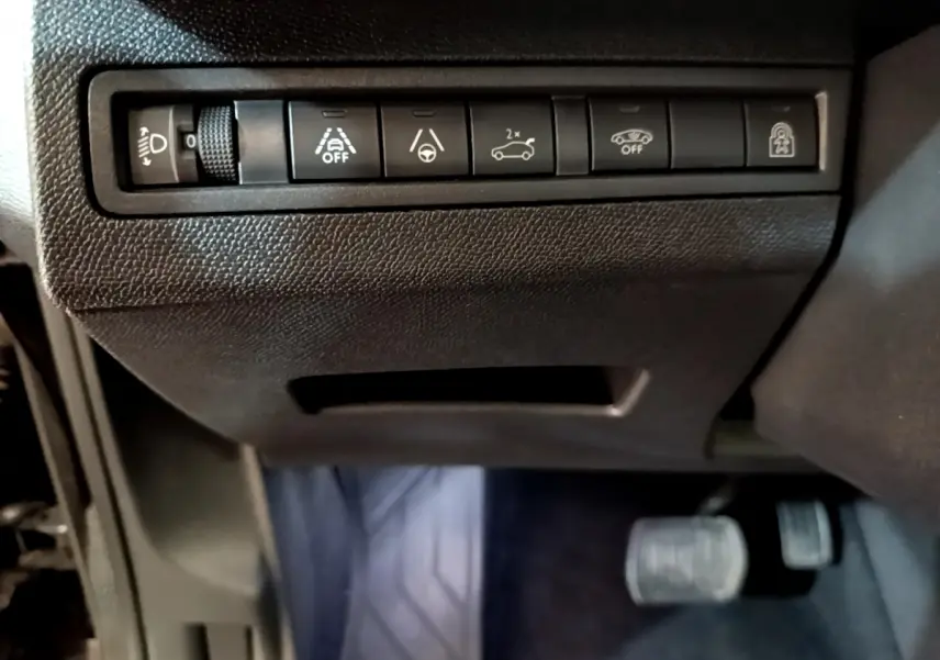 Gros plan sur les commandes d'assistance et réglage des phares du tableau de bord noir du Peugeot 3008 2022.