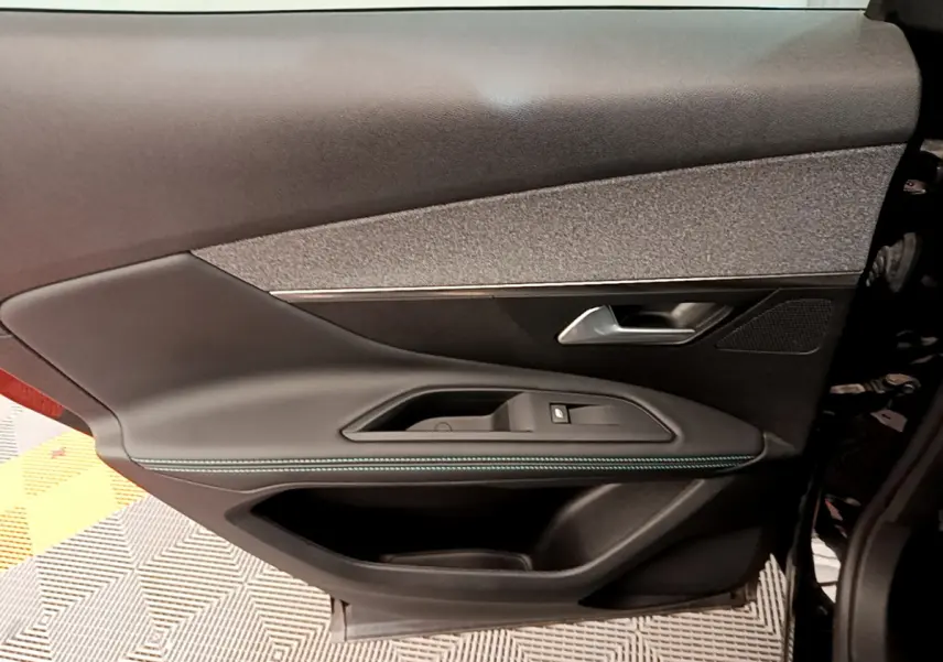 Gros plan sur la porte côté gauche intérieure du Peugeot 3008 noir, avec garniture tissu et surpiqûres bleues.