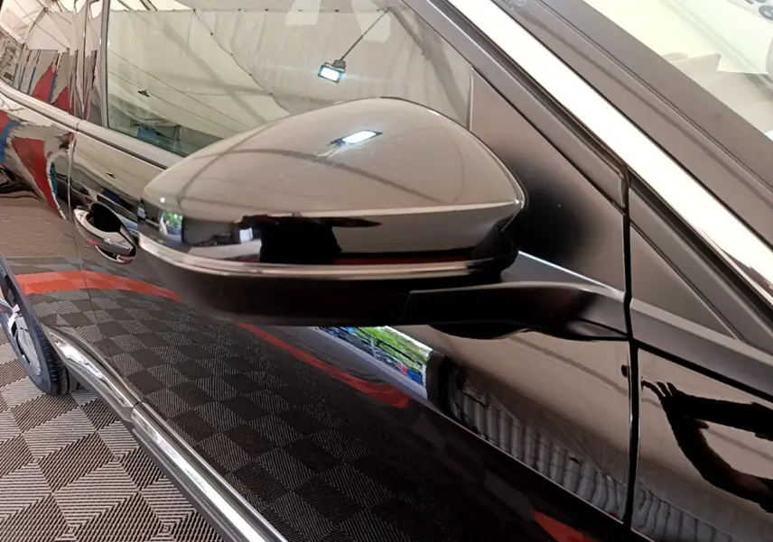 Gros plan sur le rétroviseur côté gauche d'un Peugeot 3008 noir brillant, reflétant l'environnement intérieur.