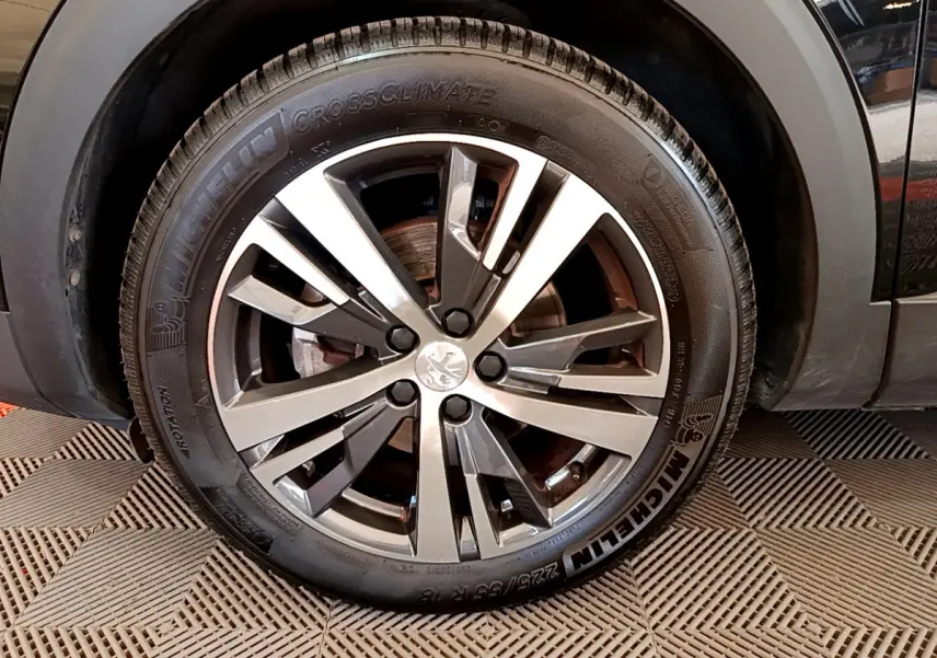 Gros plan sur la roue avant gauche du Peugeot 3008 noir, mettant en valeur la jante alliage et le pneu Michelin CrossClimate.