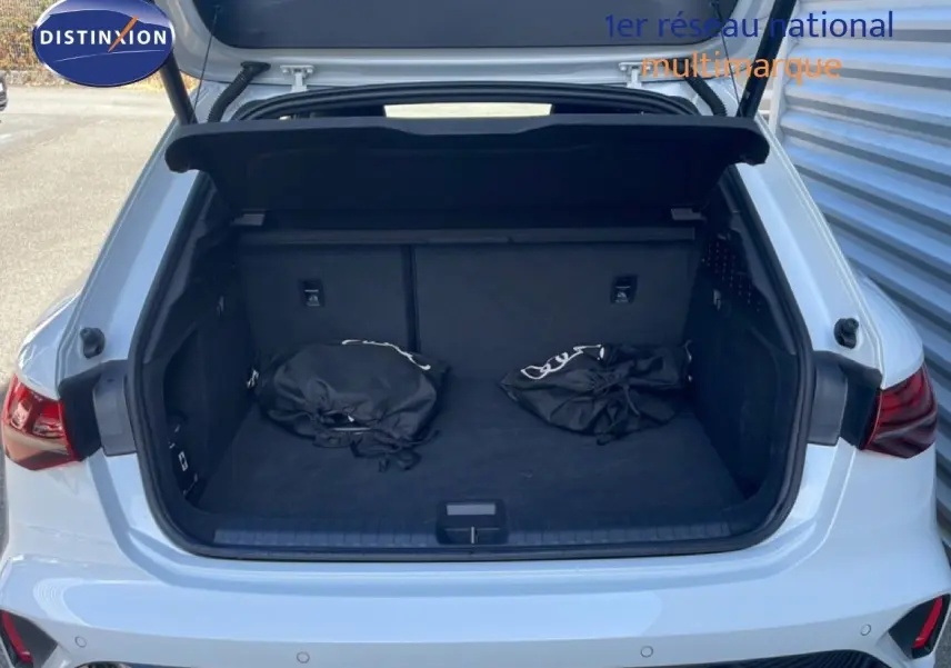 Coffre ouvert vu de l'arrière d'une Audi A3 Sportback blanc ibis 2025 avec deux sacs noirs à l'intérieur.
