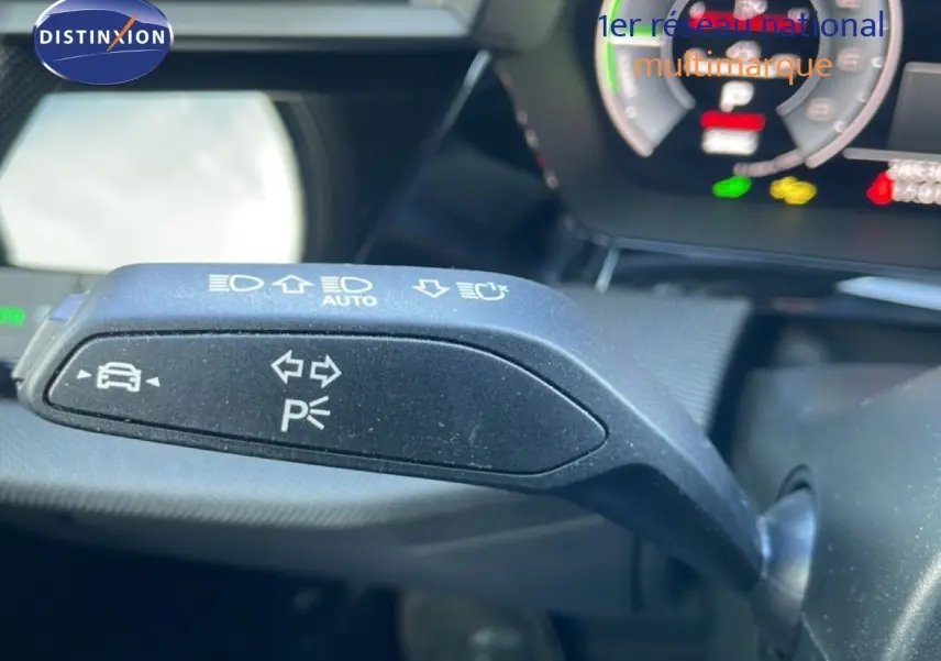 Gros plan sur la commande de clignotants et feux automatiques à gauche du volant dans l'Audi A3 Sportback blanc ibisé 2025.