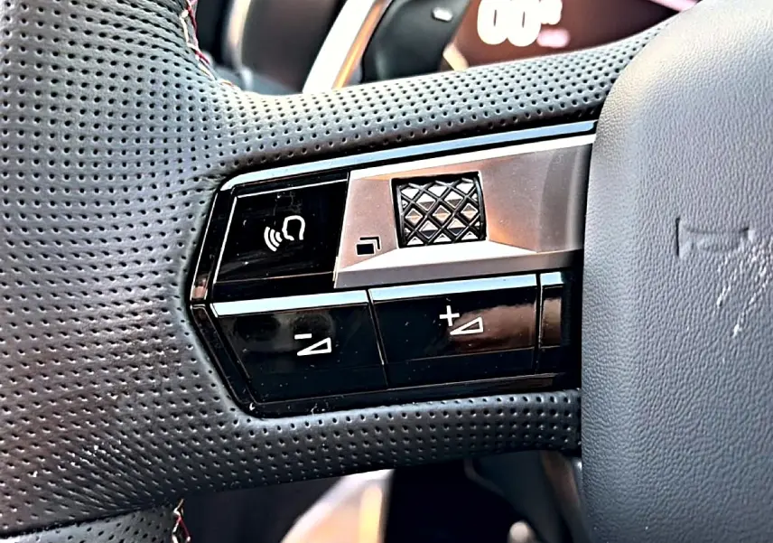 Gros plan sur les commandes noires et argentées à gauche du volant perforé du DS7 noir 2026.