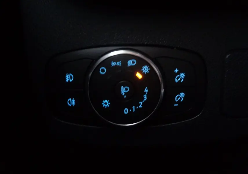 Gros plan sur la commande d'éclairage du Ford Puma blanc 2022, avec voyants bleus et orange allumés.