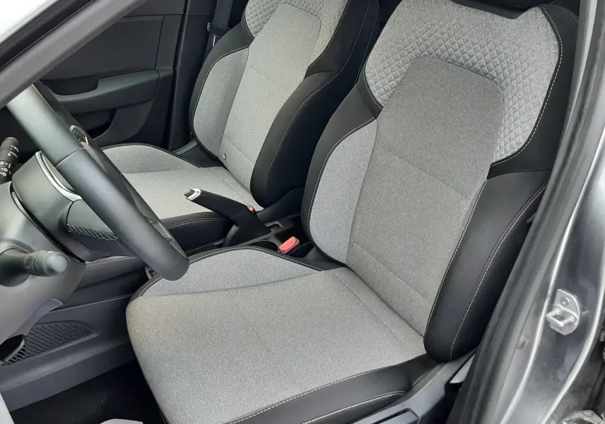 Vue intérieure côté conducteur de la Renault Clio V TCE 90ch Evolution 2025, sièges tissu gris clair avec surpiqûres noires.