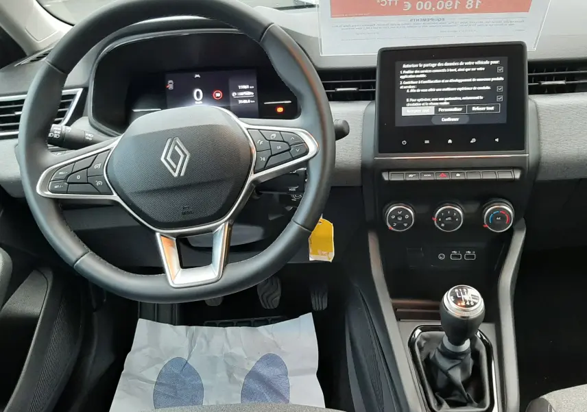 Vue intérieure avant centrée sur le volant Renault et la console centrale avec boîte manuelle dans une Clio V gris schiste 2025.