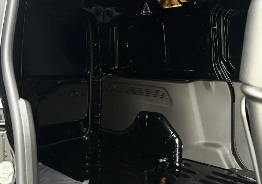 Vue intérieure de la zone de chargement noire du Citroën Berlingo Van XL 2025, avec cloison et porte latérale ouverte.