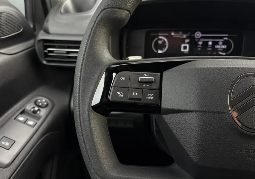 Gros plan sur le volant multifonctions noir du Citroën Berlingo 2025 avec commandes de régulateur et tableau de bord numérique.