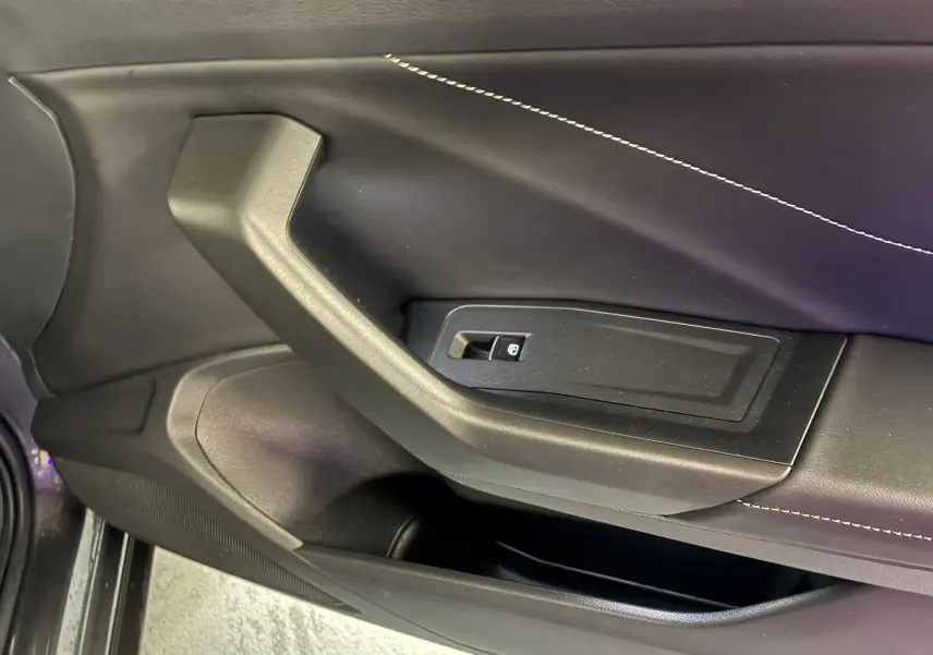 Détail de la poignée intérieure côté gauche de la porte noire du Volkswagen T-Roc 1.5 TSI 2023 avec bouton de commande de vitre.