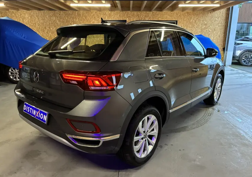 Vue 3/4 arrière droite d'un Volkswagen T-Roc gris 2023 avec feux arrière allumés dans un garage.
