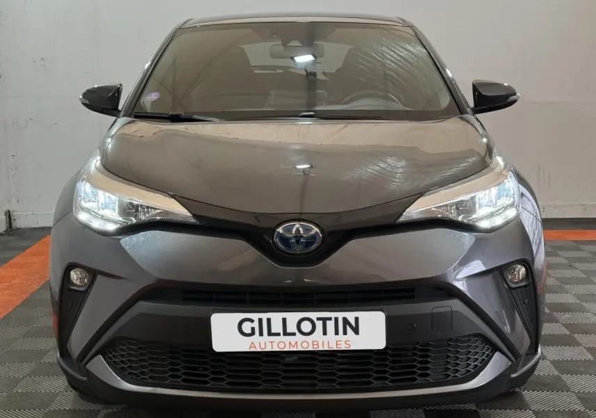 Vue frontale d'une Toyota C-HR 1.8 Hybride 122 Edition gris foncé avec phares LED allumés et calandre noire.