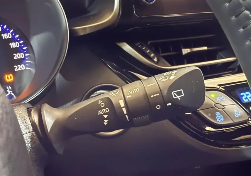 Gros plan sur la commande d’essuie-glace à gauche du volant du Toyota C-HR gris foncé, avec tableau de bord partiellement visible.