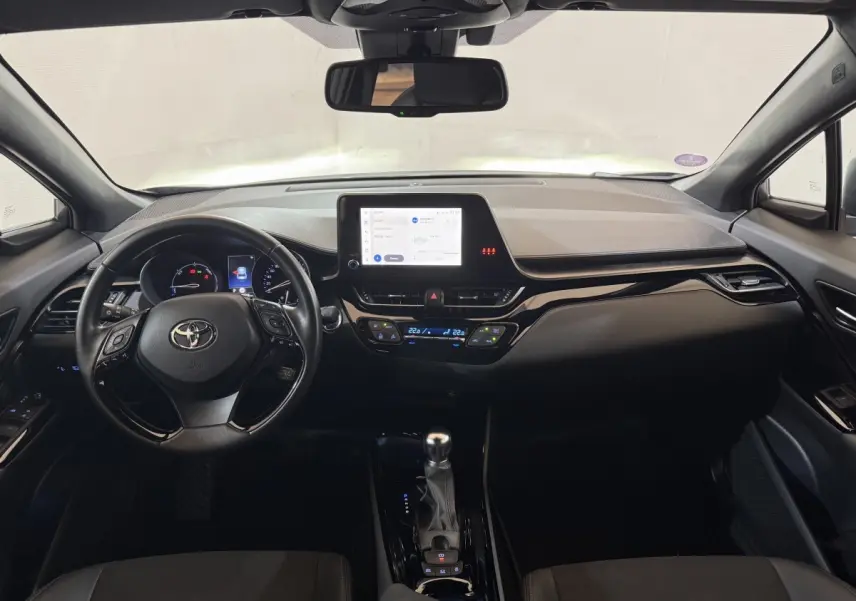 Vue intérieure frontale du tableau de bord noir du Toyota C-HR 1.8 Hybride 2022 avec écran tactile central et volant multifonctions.