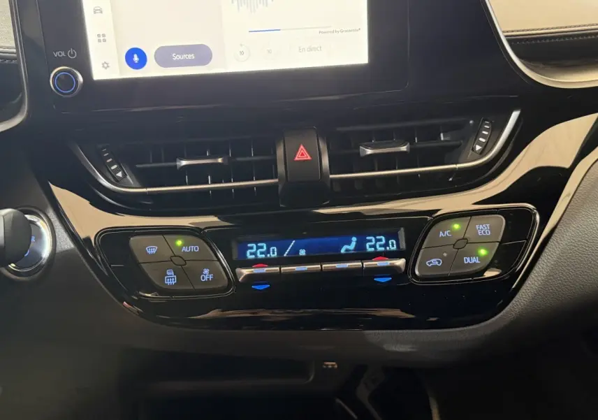Vue rapprochée du tableau de bord noir du Toyota C-HR 1.8 Hybride 2022, montrant la climatisation digitale à double zone.