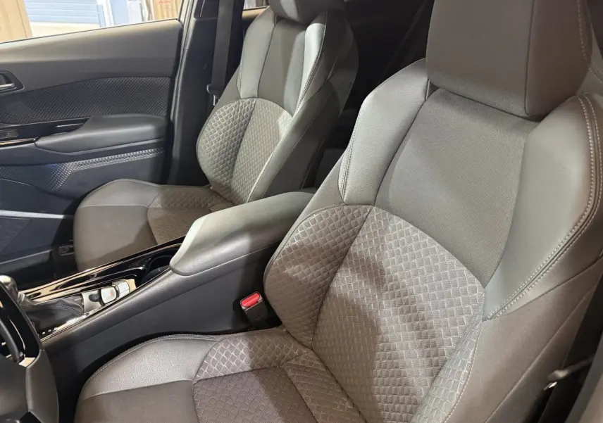 Vue intérieure rapprochée des sièges avant gris foncé avec console centrale brillante du Toyota C-HR 2022 hybride.