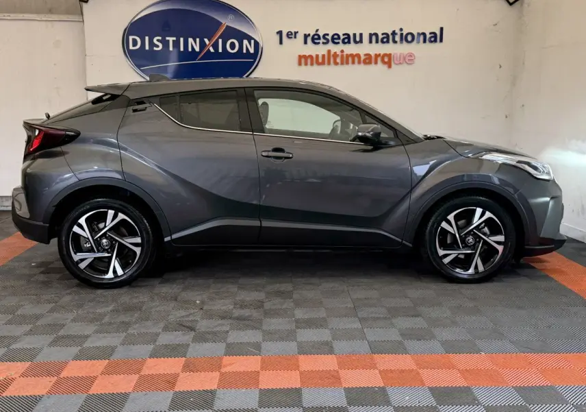 Toyota C-HR 1.8 Hybride gris foncé vu de profil côté gauche, avec jantes alliage et toit noir contrasté.