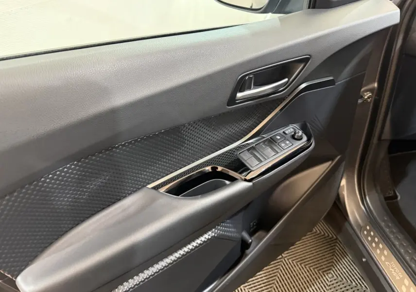 Vue intérieure du panneau de porte avant gauche du Toyota C-HR gris foncé, avec commandes électriques des vitres et poignée intégrée.