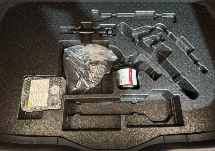 Vue plongeante sur le rangement noir dans le coffre du Toyota C-HR gris foncé, avec outils et kit de réparation pneus.