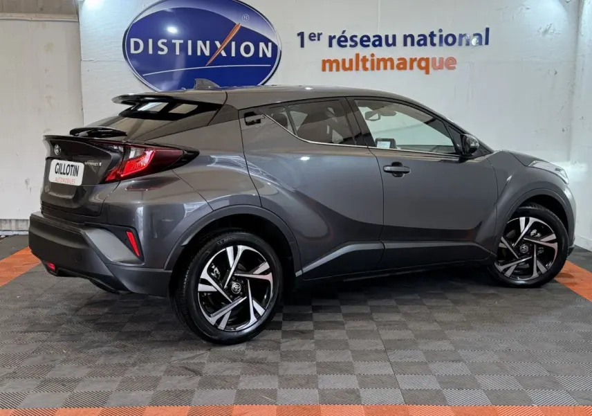 Vue latérale droite d’un Toyota C-HR 1.8 Hybride gris foncé avec jantes alliage et toit noir en arrière-plan showroom.