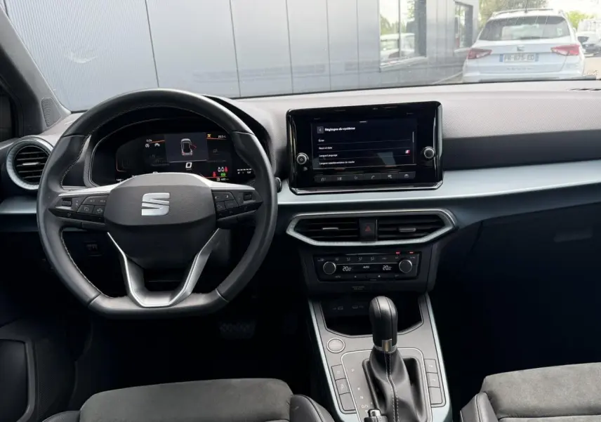 Vue intérieure avant du SEAT Arona 2025 avec tableau de bord noir, volant multifonction et écran tactile central.