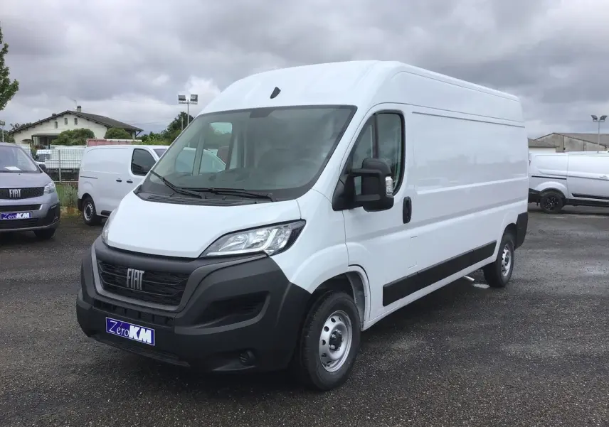 Fiat Ducato Fourgon blanc vu en 3/4 avant droit sur parking, avec calandre noire et rétroviseurs noirs.