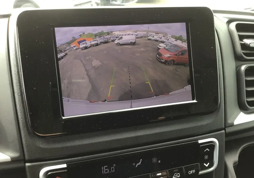 Écran tactile 7'' affichant la caméra de recul du FIAT Ducato blanc, vue arrière sur un parking avec plusieurs véhicules.