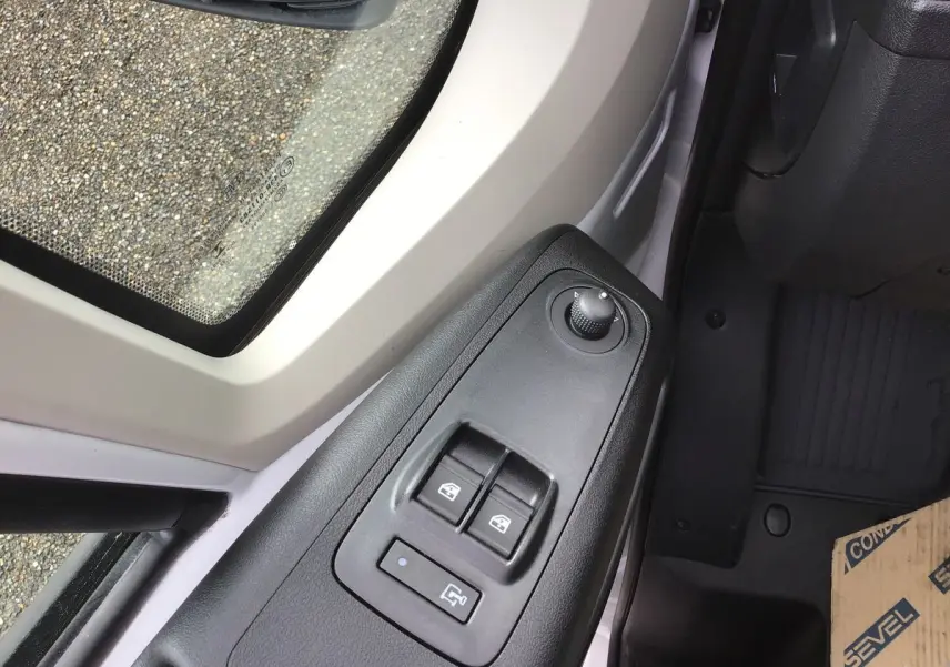 Gros plan sur les commandes de lève-vitres et réglage des rétroviseurs côté conducteur du Fiat Ducato blanc 2023.