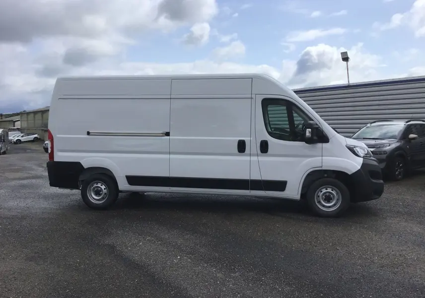 Fiat Ducato Fourgon blanc vu de profil côté gauche sur parking, avec porte coulissante et pare-chocs noirs.