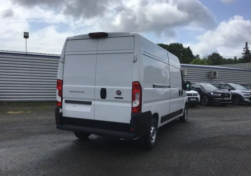 Vue 3/4 arrière d'un utilitaire FIAT Ducato blanc stationné, avec portes arrière fermées et feux rouges visibles.