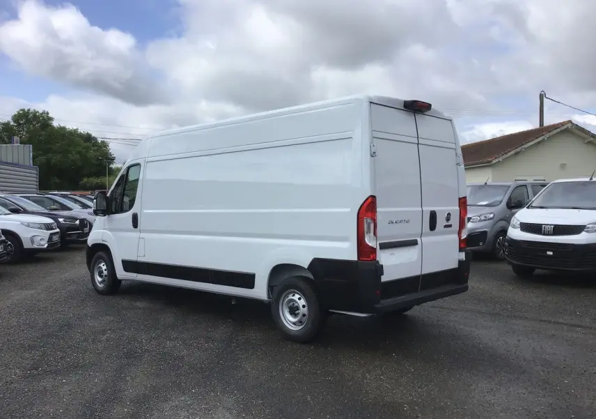 Fiat Ducato Fourgon blanc vu en 3/4 arrière droit sur un parking, avec portes arrière fermées et jantes acier.