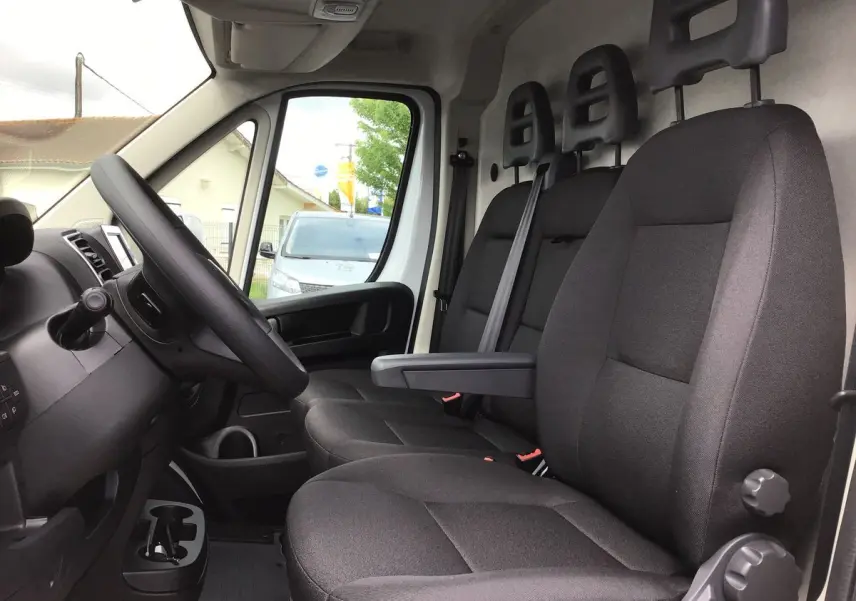 Vue intérieure côté conducteur du FIAT Ducato Fourgon blanc 2023, montrant les sièges noirs et le tableau de bord technologique.