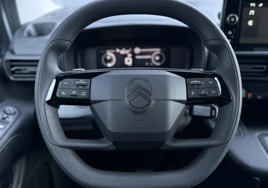 Vue rapprochée du volant multifonctions noir du Citroën Berlingo 2025 avec tableau de bord digital en arrière-plan.