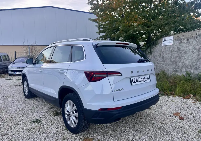 Vue 3/4 arrière droite d'un SUV SKODA KAROQ blanc 2024 avec vitres teintées et barres de toit.