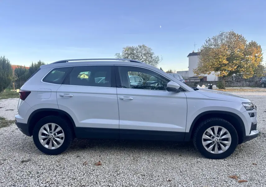 Vue de profil côté gauche d'un Skoda Karoq blanc 2024 sur un sol gravillonné en extérieur.