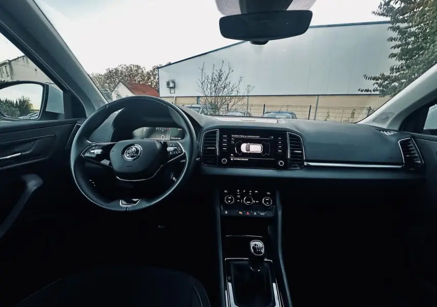 Intérieur noir du Skoda Karoq 2024 vu de face, volant multifonctions et écran tactile affichant l'aide au stationnement.