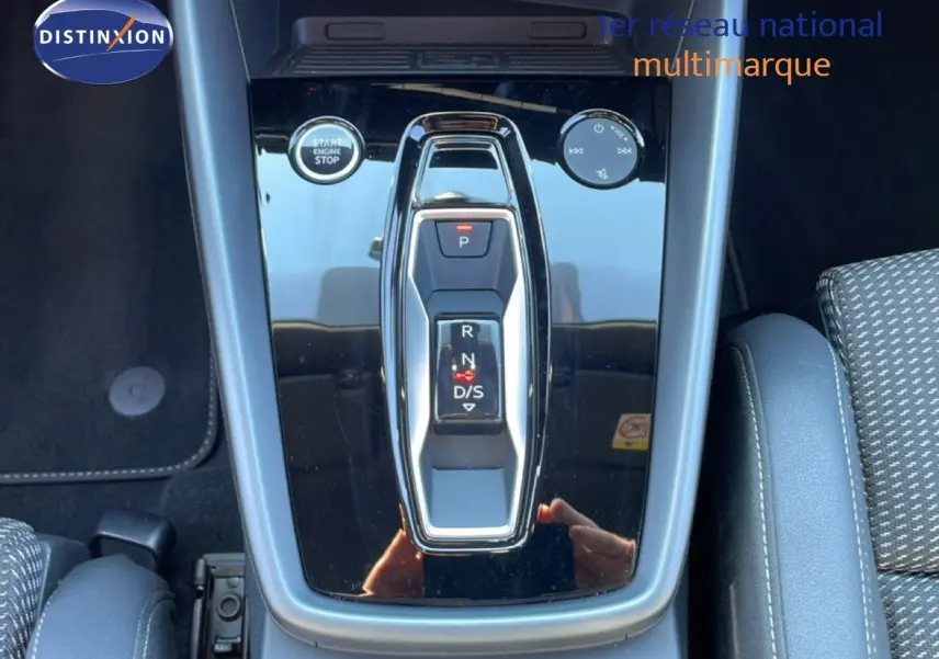 Vue rapprochée de la console centrale noire brillante avec sélecteur de boîte automatique et bouton start/stop dans un Audi A3 Sportback bleu Navarre.